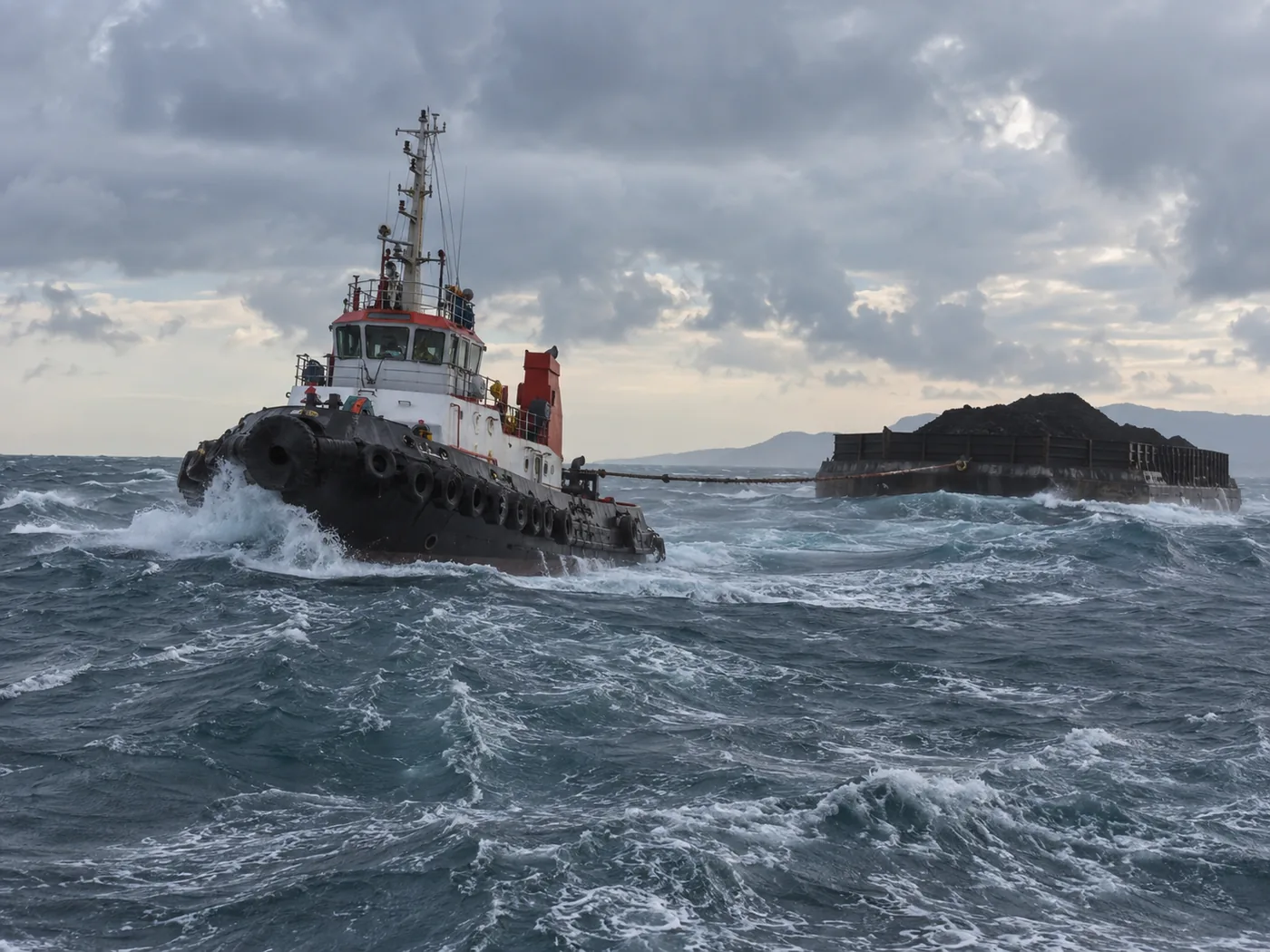 Tugboat towing a loaded barge through heavy seas